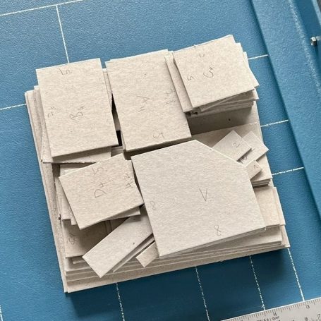 Stapel von rechteckigen, grauen Papierblättern auf blauer Unterlage.