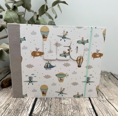 Ein fröhliches Notizbuch mit Luftballons und Flugzeugen auf einem gemusterten Cover.